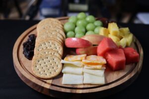 Wooden platter with crackers, cheese, grapes, fruit, and dried berries